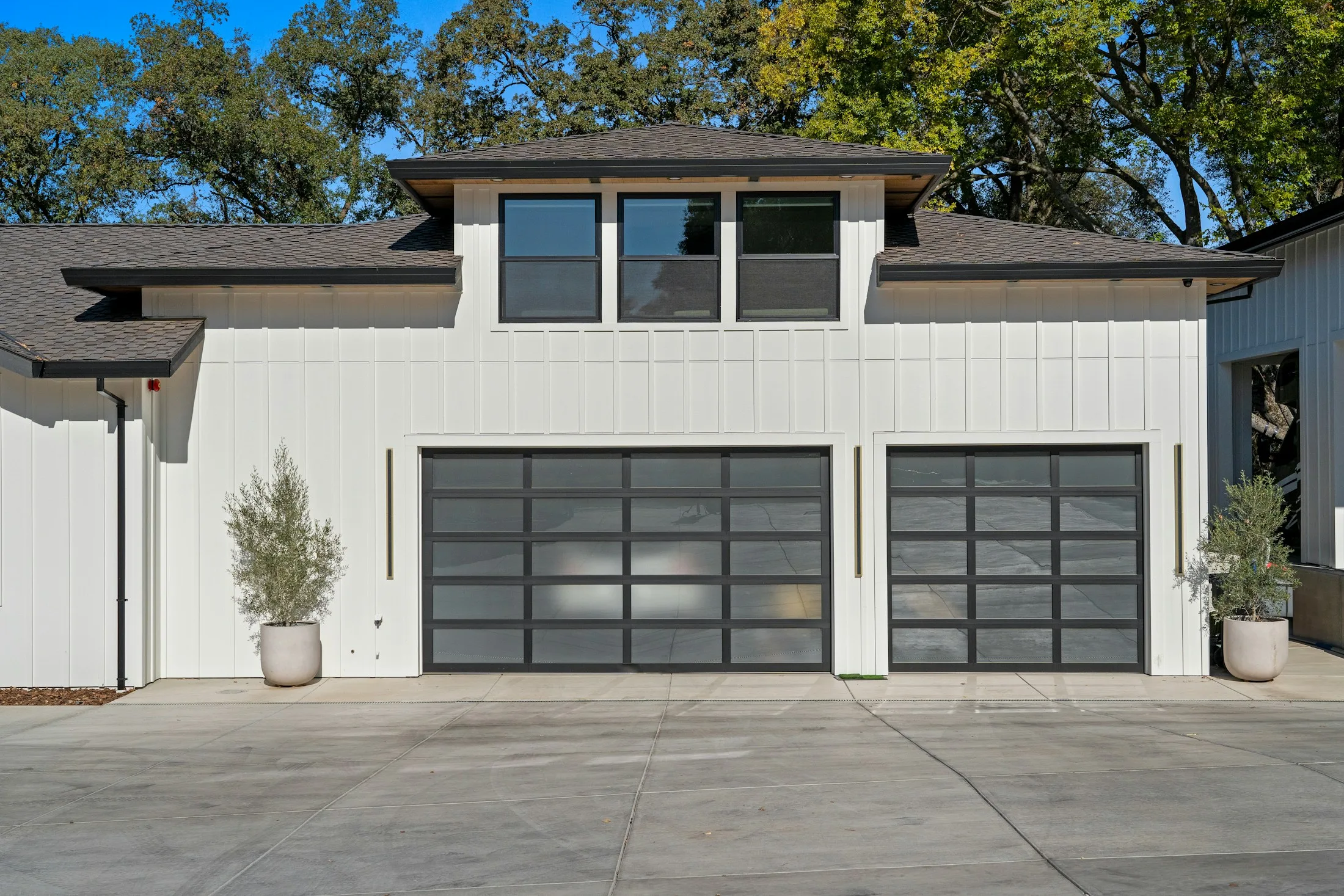 Two dark-framed glass garage doors on a white home, shown in full from the driveway.