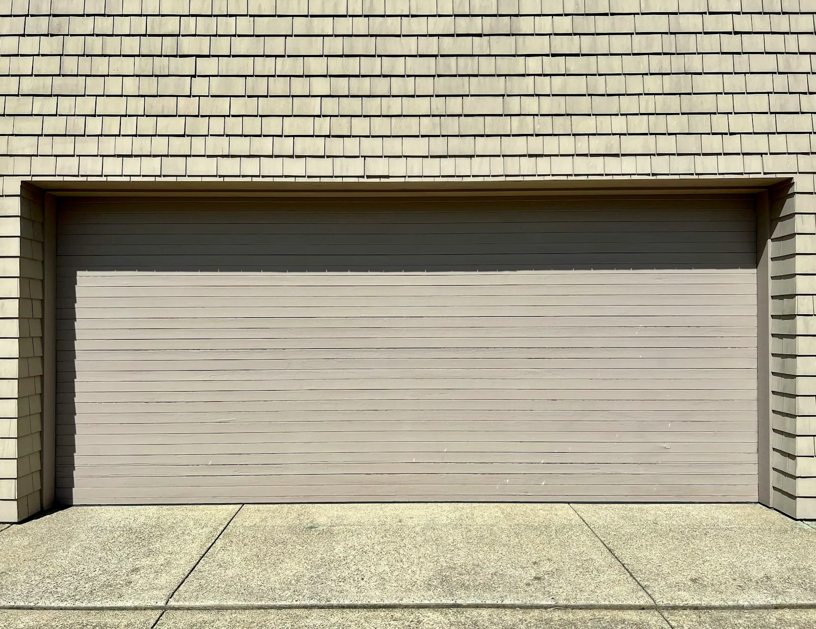 A wide garage door with closely spaced horizontal lines beneath shingle siding.